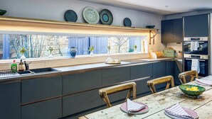 A modern kitchen with a large window, built-in appliances, and a dining area with a wooden table and chairs. - The Dairy & Annex - UKC7805 (Brinkburn Priory)