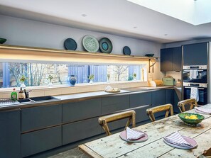 Eine moderne Küche mit großem Fenster, integrierten Geräten und einem Essbereich mit Holztisch und Stühlen.