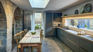 A modern kitchen with a skylight, stone archway, and a dining area with a wooden table and chairs. - The Dairy & Annex - UKC7805 (Brinkburn Priory)