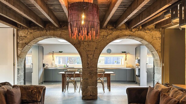 A spacious living area with a stone column, two sofas, a dining table, and a kitchen visible through an archway. - The Dairy & Annex - UKC7805 (Brinkburn Priory)