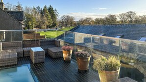A rooftop terrace with wicker furniture, potted plants, and a glass balustrade overlooking a green landscape. - The Dairy & Annex - UKC7805 (Brinkburn Priory)