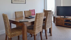 A dining area with a wooden table and wicker chairs, a framed inspirational quote on the wall, and a television on a wooden stand. - 2 bedroom accommodation in Torquay (Torquay)