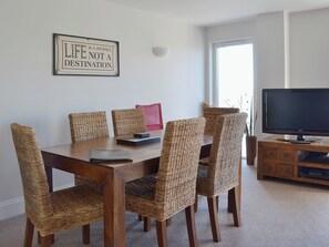 A dining area with a wooden table and wicker chairs, a framed inspirational quote on the wall, and a television on a wooden stand. - 2 bedroom accommodation in Torquay (Torquay)