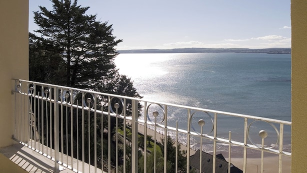 Ein Balkon mit Metallgeländer, der auf einen Strand und den Ozean blickt.