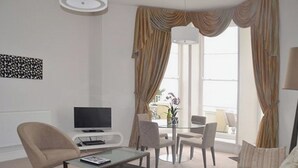 Ein modernes Wohnzimmer mit Flachbildfernseher, Glastisch, einer Couch und einem Essbereich mit Stühlen.