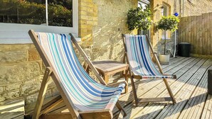 Deux fauteuils de jardin à rayures, placés sur une terrasse en bois, avec un mur en pierre et des plantes en pot en arrière-plan.