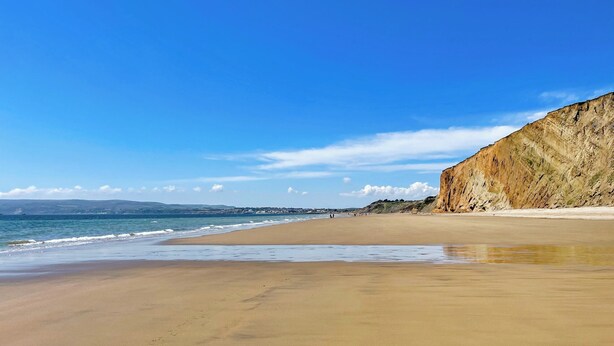 Une vaste plage de sable bordée d’une falaise abrupte d’un côté et offrant une vue sur un ciel bleu et dégagé.