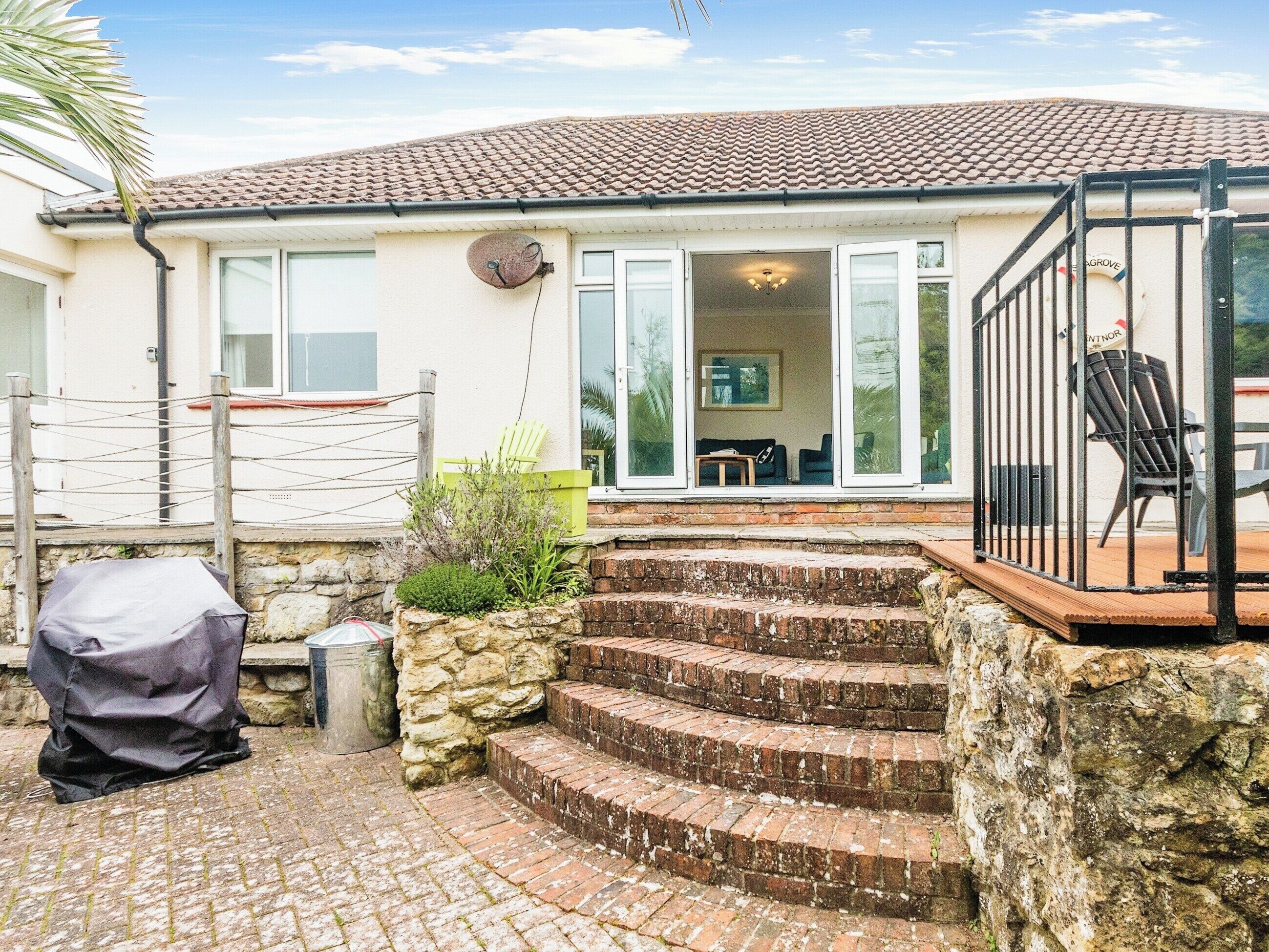 A house with a tiled roof, a covered patio area with steps leading to a deck, and a fenced garden.