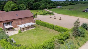 Une ferme située en zone rurale, avec une grange en briques, un espace extérieur aménagé pour s’asseoir et un enclos clôturé pour les chevaux.