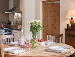 A dining table set with plates, cutlery, a vase with flowers, a bowl of strawberries, and a bottle of Fentimans lemonade. - The Hayloft - UKC3678 (Tattersett, near Fakenham)