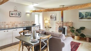A cozy living room with a fireplace, a dining area with a table set for two, and a kitchen with a tiled backsplash. - The Old Feedhouse - UKC3679 (Tattersett, near Fakenham)