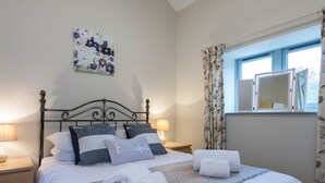 A neatly made bed with white and grey bedding, two bedside lamps, a floral artwork on the wall, and a window with curtains. - The Milking Parlour - UKC3681 (Tattersett, near Fakenham)