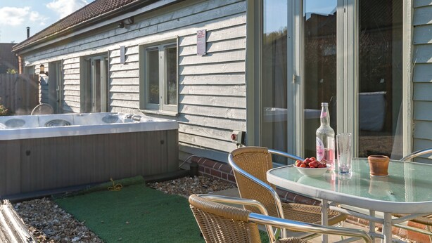 A house with a patio area featuring a glass table, wicker chairs, and a hot tub. - The Milking Parlour - UKC3681 (Tattersett, near Fakenham)