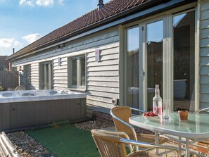 Een huis met een patio, voorzien van een glazen tafel, rieten stoelen en een jacuzzi.