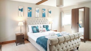 A bedroom with a tufted headboard, a bed with white linens and decorative pillows, a blue throw blanket, and a wooden nightstand with a lamp. - The Stables - UKC3684 (Tattersett, near Fakenham)