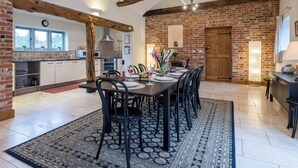 A spacious kitchen with exposed brick walls, a dining area with a long table set for six, and a rustic ceiling with wooden beams. - The Stables - UKC3684 (Tattersett, near Fakenham)