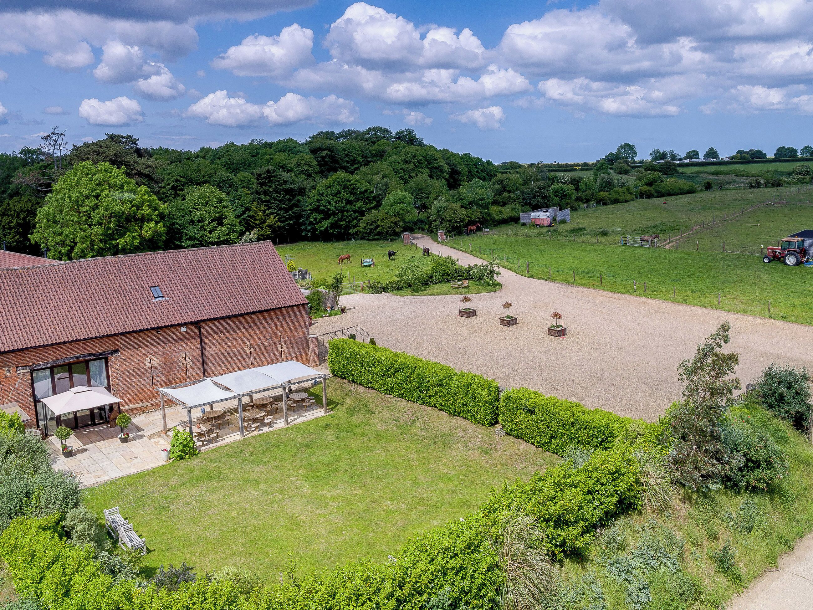 A rural farmstead with a brick barn, outdoor seating area, and a fenced horse paddock.