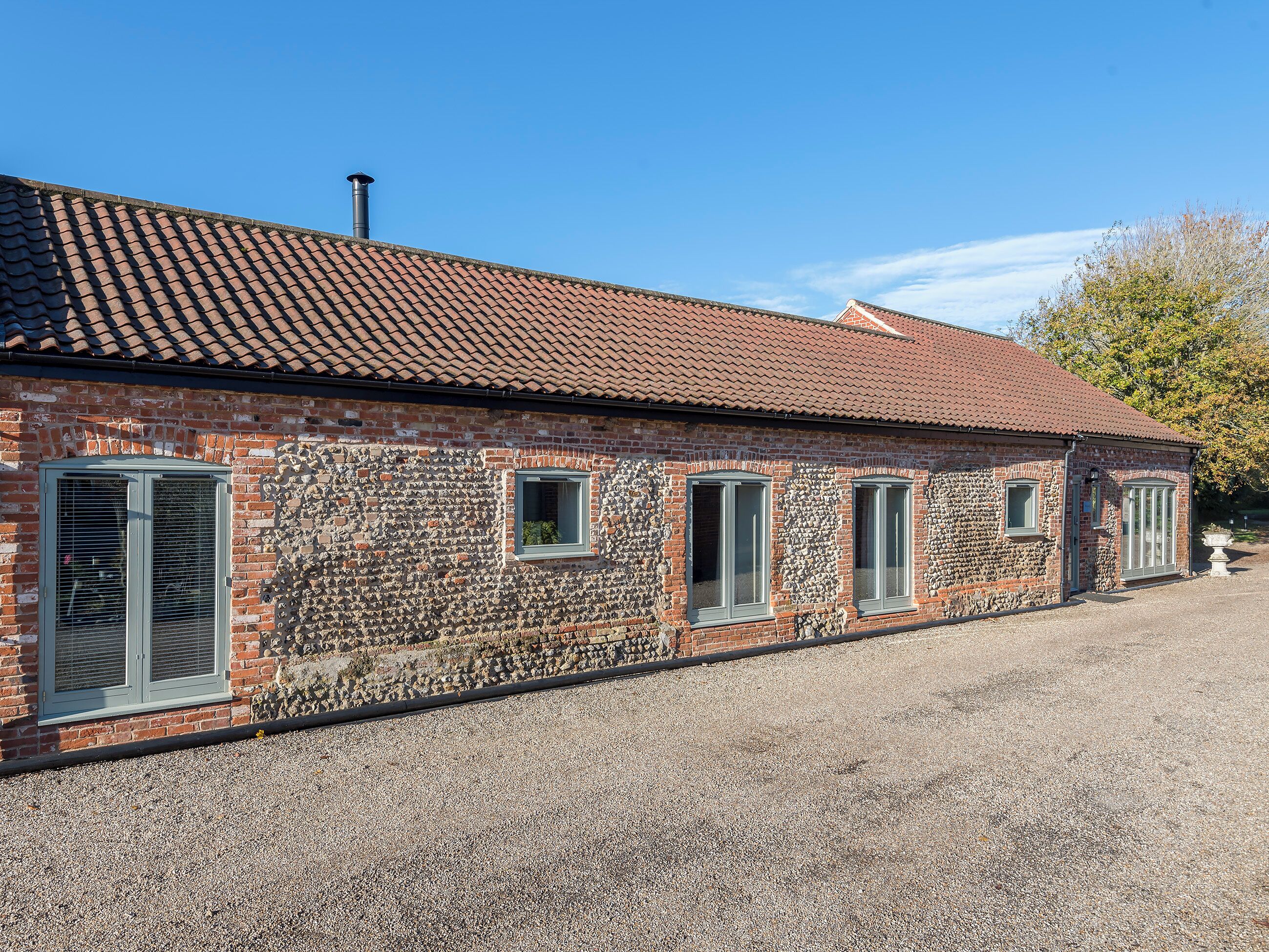 A brick building with a tiled roof, stone wall, and gravel driveway.