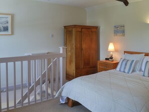 Ein Schlafzimmer mit einem Bett, einem Holzschrank, einem Nachttisch mit Lampe, einem gerahmten Bild an der Wand und einer Treppe.