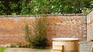 A brick wall, a wooden hot tub, and a small garden area with a curved pathway. - 3 bedroom accommodation in Worstead, near North Walsham (Worstead, near North Walsham)