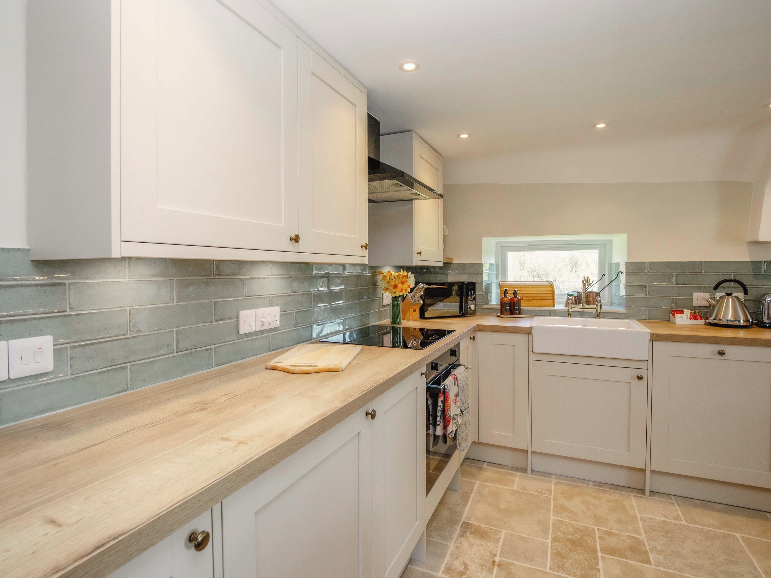 A modern kitchen with white cabinets, a wooden countertop, a built-in oven, and a window providing natural light.