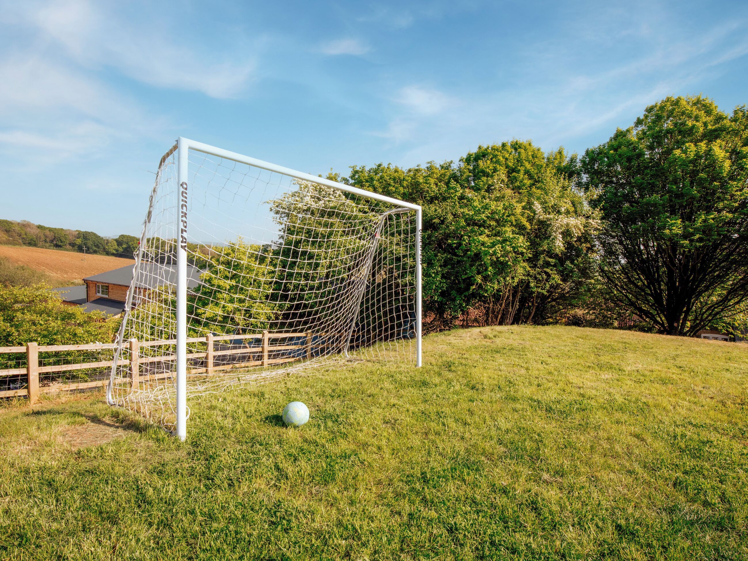 A soccer goal in a grassy field with trees and a building in the background.