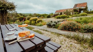 Een picknicktafel met een taart en theekopjes, omringd door een tuin met een huis op de achtergrond.