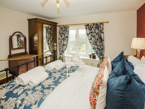 Ein Schlafzimmer mit einem Bett, einer Kommode, einem Spiegel, einem Fenster mit Vorhängen und einem Nachttisch mit Lampe.