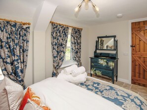 Ein Schlafzimmer mit Bett, Vorhängen, einem Schminktisch, einem Spiegel und einer Holztür.