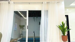 Ein Zimmer mit einer Schiebeglastür, die zu einem Poolbereich führt, einer Topfpflanze und einem Deckenventilator.