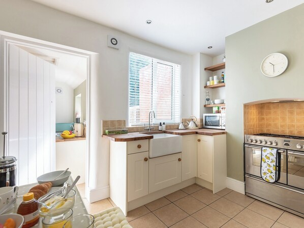 A modern kitchen with white cabinets, a built-in oven, a microwave, and a window with blinds.