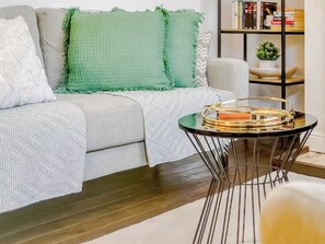 A modern living room with a grey sofa, green throw pillows, a patterned throw blanket, and a small round table with a tray.