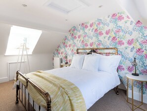 A bedroom with a bed, a nightstand, a lamp, a radiator, and a window with a ladder.