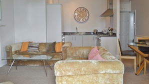 A living room with a sofa, a glass coffee table, a dining table with chairs, a kitchen area with cabinets and a clock on the wall. - 2 bedroom accommodation in Torquay (Torquay)