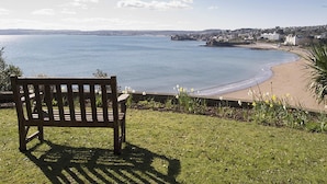 A bench overlooking a beach with a view of the sea and distant buildings. - 2 bedroom accommodation in Torquay (Torquay)