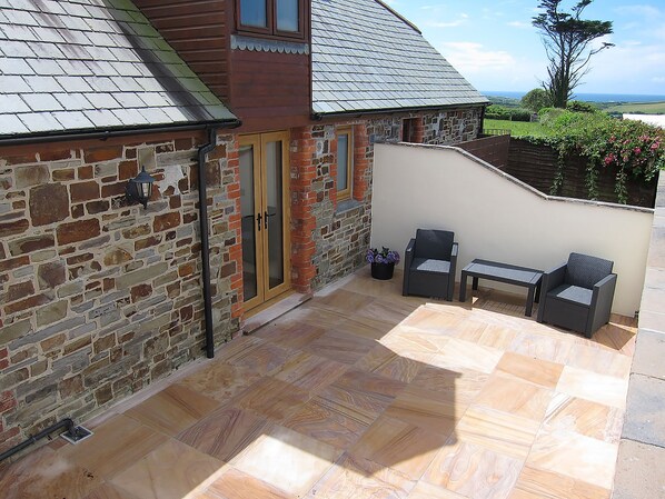 A stone building with a wooden door, a small patio with a table and chairs, and a view of the countryside. - 1 bedroom accommodation in Marhamchurch, near Bude (Marhamchurch, near Bude)