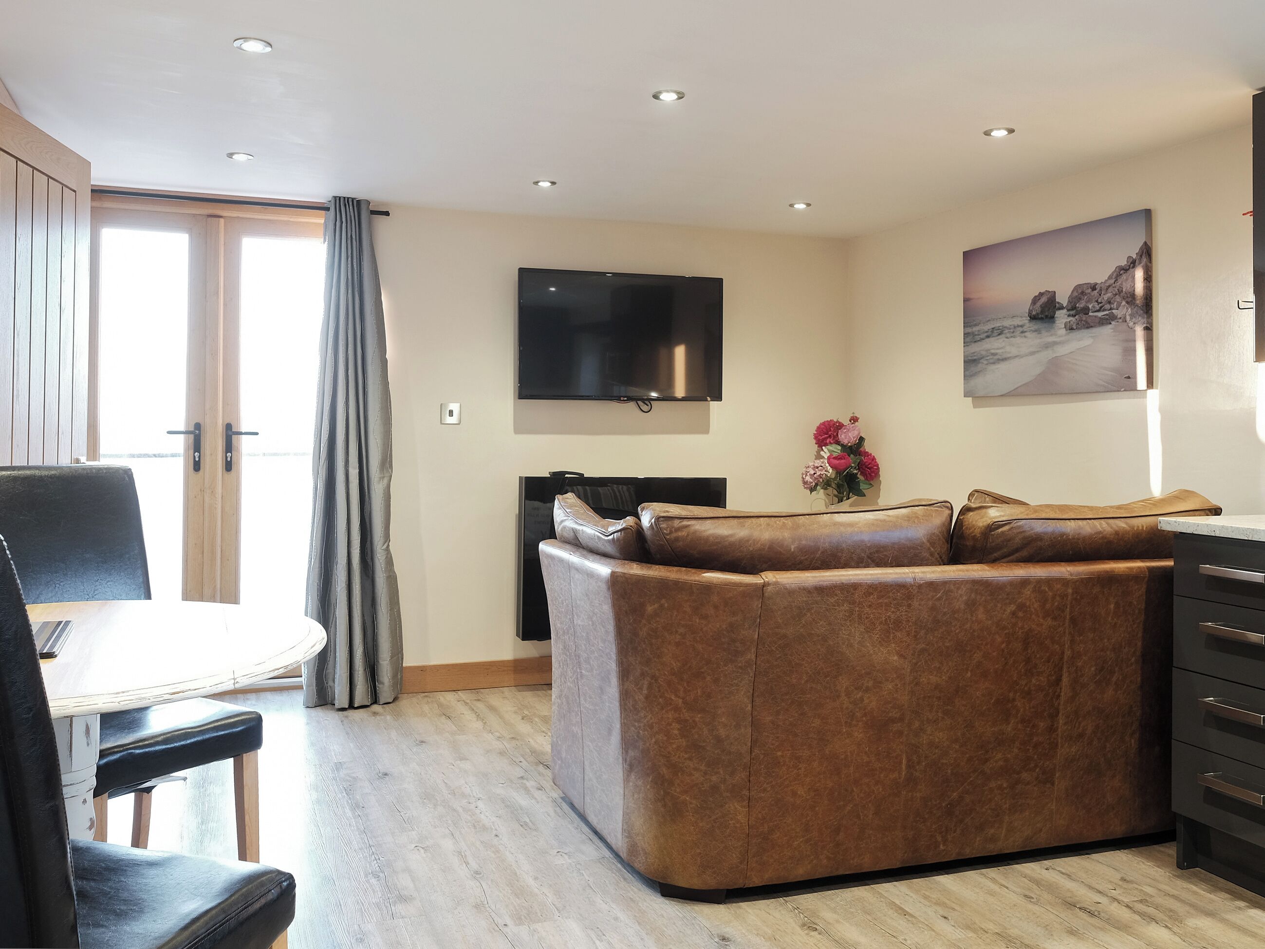 Un salon moderne avec un canapé en cuir, un téléviseur à écran plat et un coin repas comprenant une table et des chaises.
