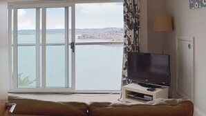 Een woonkamer met een groot raam, een flatscreen televisie op een meubel, een bank en een lamp.