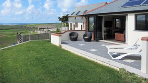 Ein modernes Haus mit Terrasse, Sitzgelegenheiten im Freien und Blick auf die Landschaft.