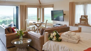 Ein Hotelzimmer mit Bett, Sofa, Esstisch, Fernseher und Blick auf die Landschaft.