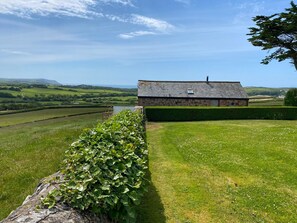 A stone building with a sloped roof, surrounded by a well-maintained hedge and a grassy field. - 1 bedroom accommodation in Marhamchurch, near Bude (Marhamchurch, near Bude)