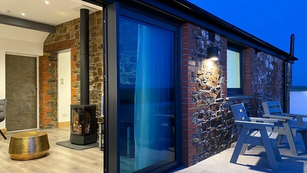 Een modern huis met een gevel van natuursteen, een glazen voordeur, een open haard en een terras.