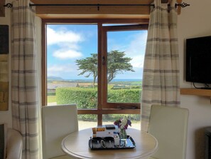 A room with a table, a chair, a TV, and a window with curtains. - 1 bedroom accommodation in Marhamchurch, near Bude (Marhamchurch, near Bude)
