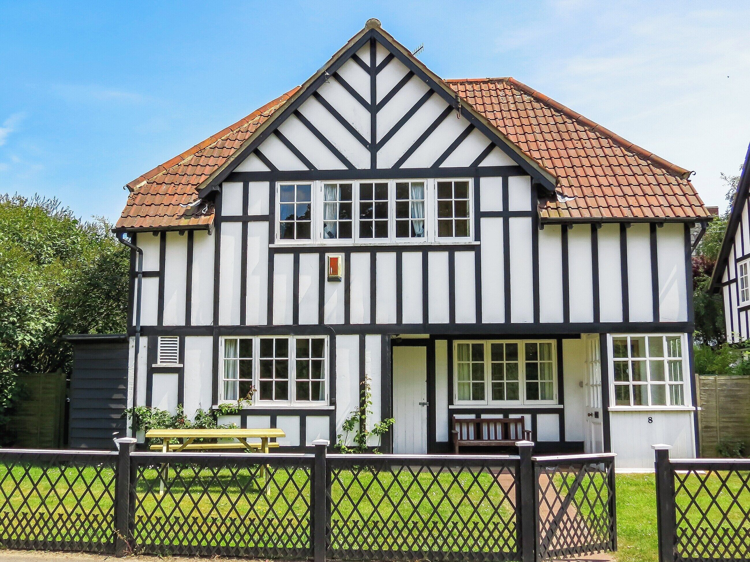 Une maison de style Tudor traditionnel, avec un toit à forte pente, de nombreuses fenêtres et une porte d’entrée.