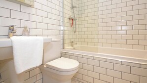 Ein Badezimmer mit weißen Fliesen, einer weißen Toilette, einem Waschbecken mit Handtuch und einer Duschkabine.