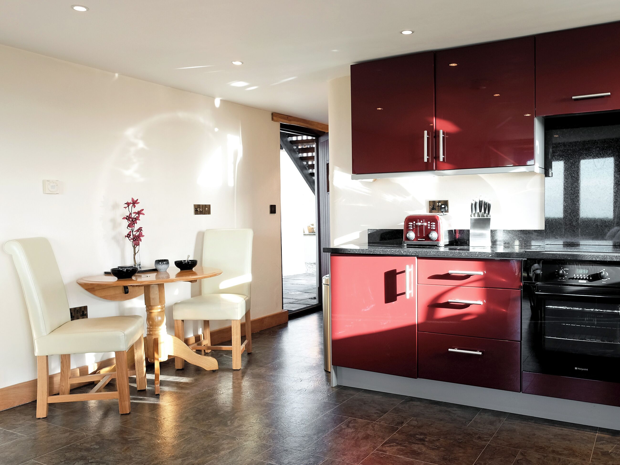 A modern kitchen with red cabinets, a black stove, and a dining area with a table and chairs.