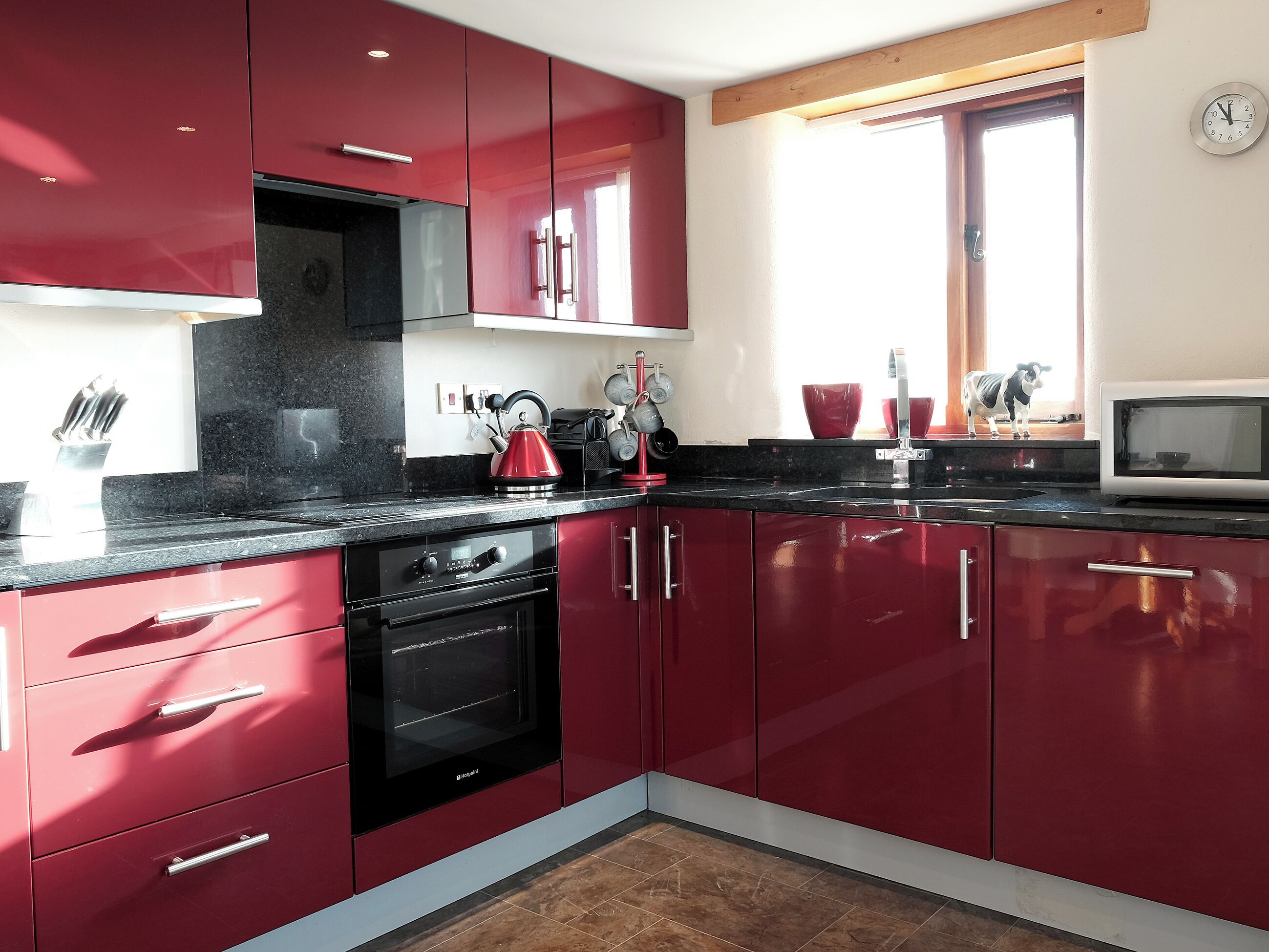 Une cuisine moderne avec des meubles rouges, une cuisinière noire et un four à micro-ondes.