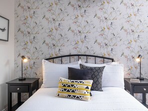A neatly made bed with white bedding, two black nightstands with lamps, and a wall with a bird pattern wallpaper. - 2 bedroom accommodation in Broseley (Broseley)