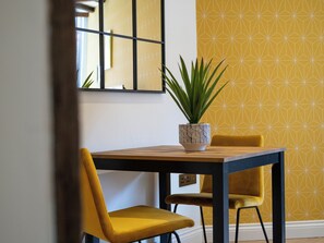 Una mesa de comedor con sillas, una planta en maceta y una pared con estampado geométrico.