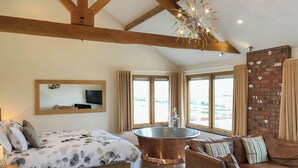 A bedroom with a bed, a large window, a bathtub, a wooden ceiling, and a brick wall. - 1 bedroom accommodation in Marhamchurch, near Bude (Marhamchurch, near Bude)